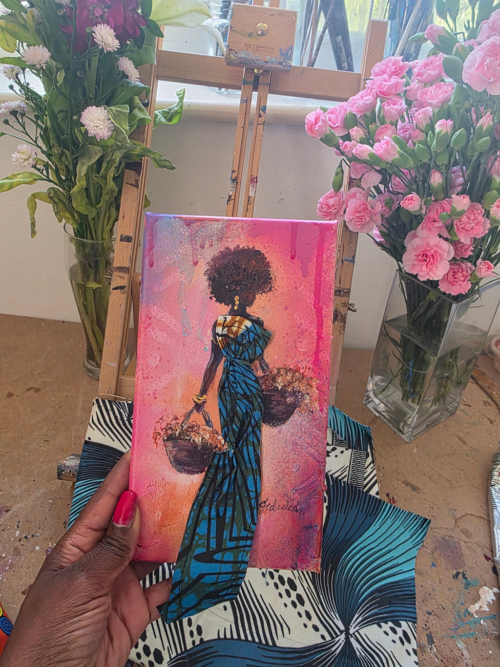 African fabric art, African artwork, mini art of a rural African woman in Jedidah Chick's art studio with flowers and fabric in the background.