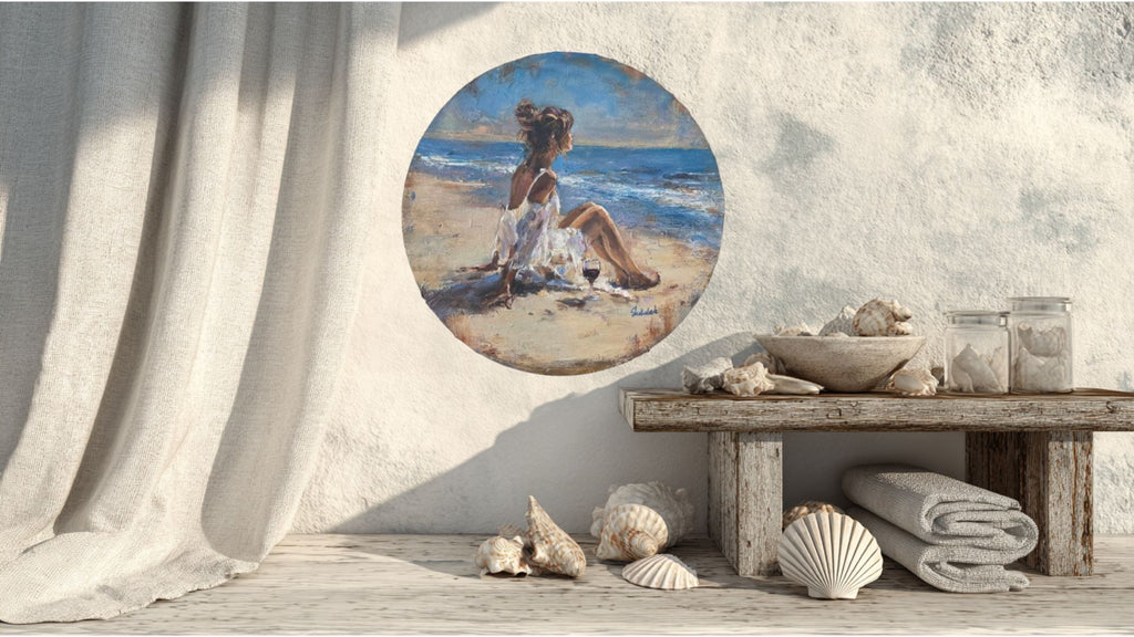 A mockup of a seascape, girl on the beach round circular painting,  with decorative items underneath.   In the painting the girl is sat with a flowing dress, on the beach with a glass of wine next to her.